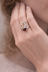 Bague Lotus en argent 925 avec pierre grenat et motif florale délicat, portée sur le doigt près du visage. Amour et vitalité.