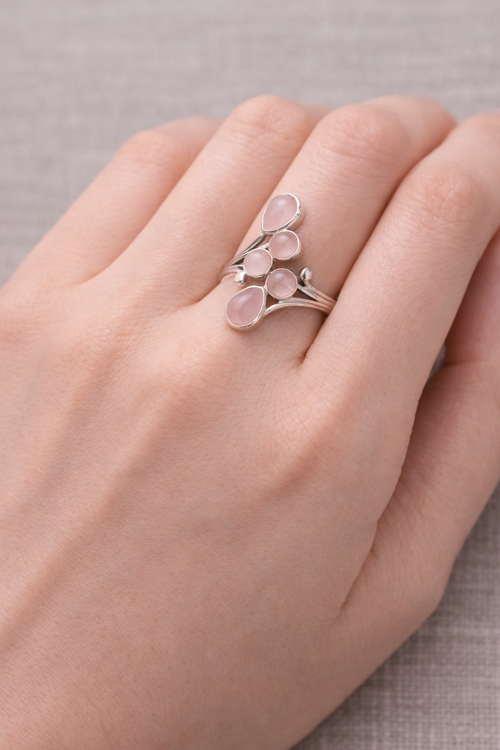 Bague Murmure du Cœur en quartz rose et argent 925 portée sur le doigt, design en pendentifs pendants délicats et pierres rose pâle.