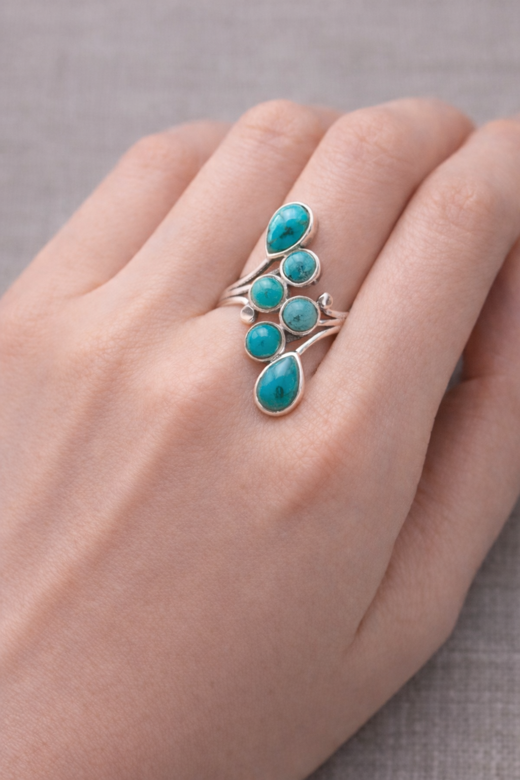 Bague Onde Céleste turquoises et argent 925 entourant plusieurs pierres turquoise sur le doigt femme.
