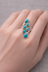 Bague Onde Céleste turquoises et argent 925 entourant plusieurs pierres turquoise sur le doigt femme.