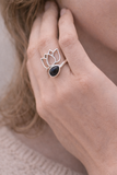 Bague Lotus Obsidienne & Argent 925, modèle Ancrage & Protection: doigt portant une bague argentée avec pierre noire et motif lotus.