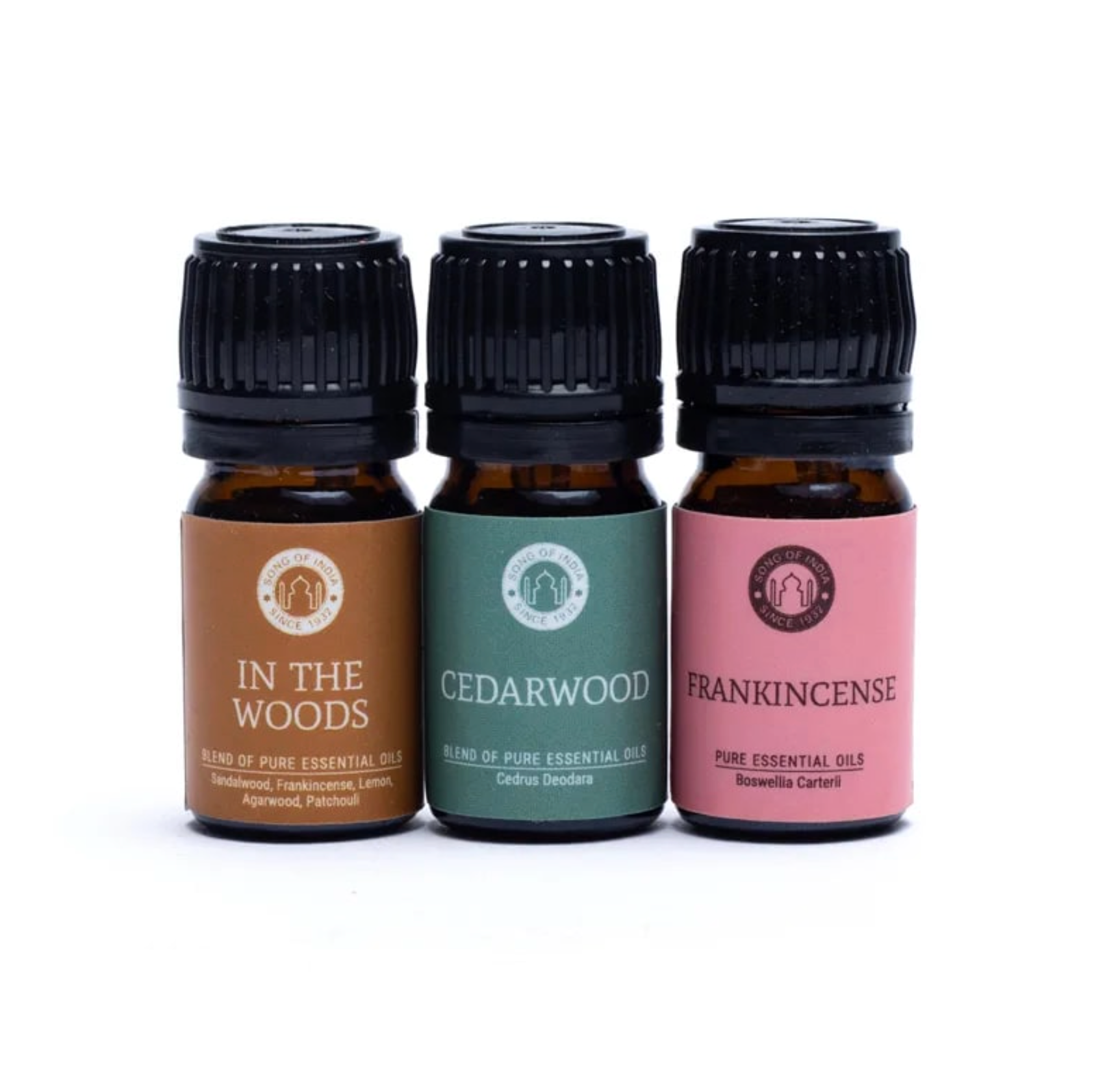 Trois fioles d’huiles essentielles alignées dans des étiquettes colorées (In The Woods, Cedarwood, Frankincense) et bouchons noirs. Coffret Huiles Essentielles Équilibre et relaxation.