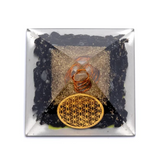 Orgonite Tourmaline noire et cristal de roche avec motif Fleur de Vie et poignée métallique orangée, posé sur lit de gravier noir. Protection énergétique.
