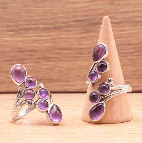 Bague argentée à cabochons améthystes violets en volutes raffinées, pieds de bague display sur socle en bois.
