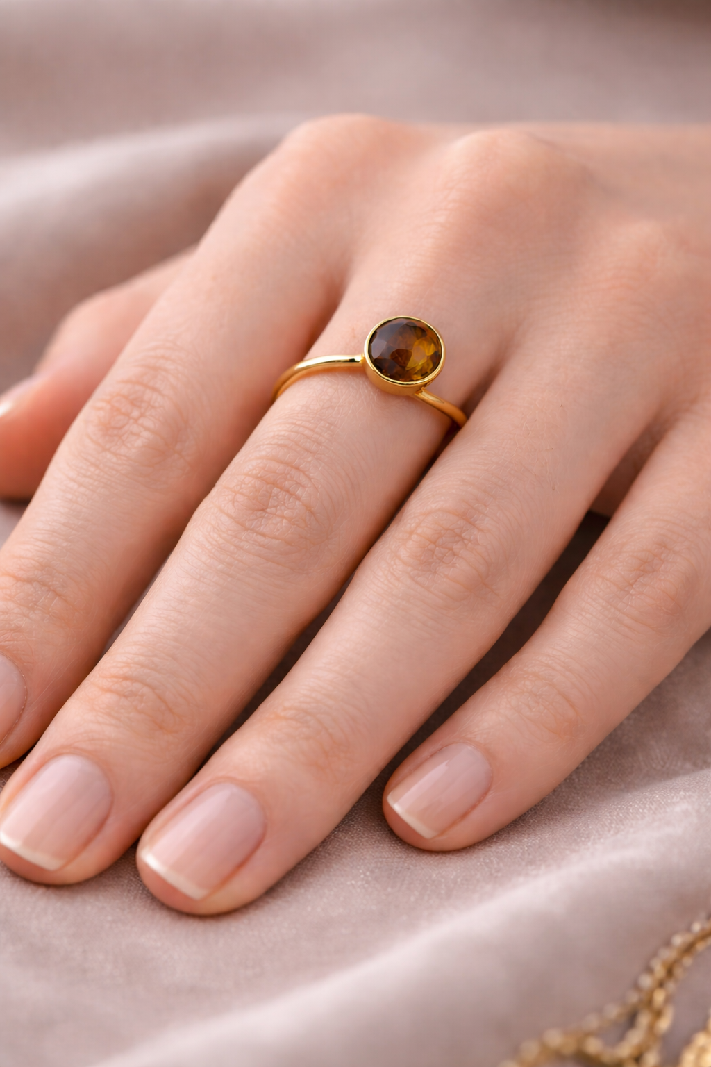 Bague œil de tigre en or jaune, portée sur un doigt, sur fond de velours rose pâle. Protection et force intérieure.
